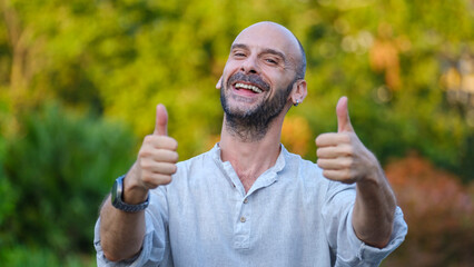 A middle-aged handsome businessman looking at the camera in a tree-lined park on a summer day,...