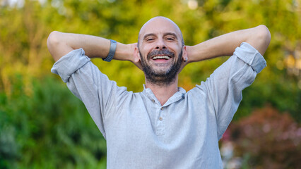 A middle-aged handsome businessman smiling and looking at the camera in a tree-lined park on a...