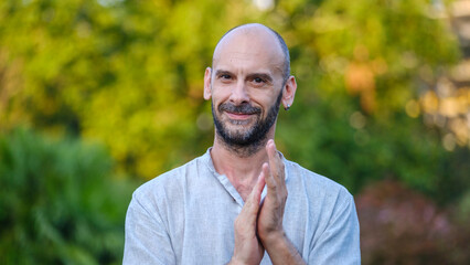 A middle-aged handsome businessman in a tree-lined park on a summer day, looking at the camera with...