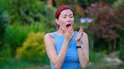 A young beautiful businesswoman looking at the camera while sneezing in a park surrounded by trees...