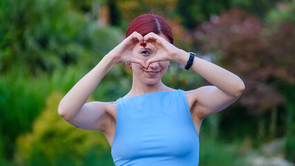 A young, beautiful businesswoman  is looking at the camera while making a heart shape with her...