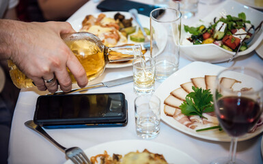 A man pours whiskey into a glass at a set table during a festive dinner, a meal in a restaurant, a cafe, close up shot