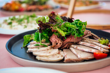 A plate with a variety of meat delicacies, decorated with lettuce leaves and microgreens. Meatloaf, roast beef, sausage. Snacks on the festive table at the event