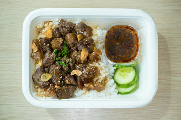 Lunch paper box with Thai beef on rice served with sauce and cucumber slice. Top view