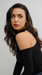 Naklejka premium In a studio setting with a white background, a young black-haired woman wearing a black blouse and jeans strikes an artistic pose