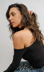 Fototapeta premium In a studio setting with a white background, a young black-haired woman wearing a black blouse and jeans strikes an artistic pose
