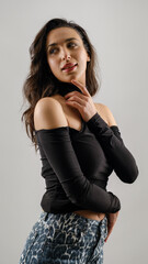 In a studio setting with a white background, a young black-haired woman wearing a black blouse and jeans strikes an artistic pose