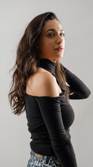 Fototapeta premium In a studio setting with a white background, a young black-haired woman wearing a black blouse and jeans strikes an artistic pose