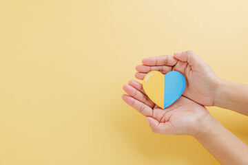 Yellow background with hands holding a divided yellow-blue heart marks Down Syndrome Day.
