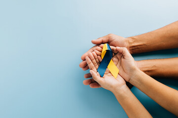 Down Syndrome awareness, hands hold a ribbon on blue background. Highlighting Down Syndrome Day