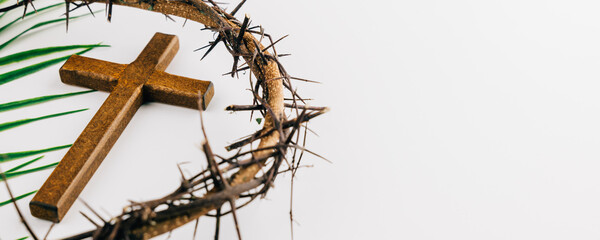 Wooden cross with crown of thorns and palm leaves on white for Palm Sunday.