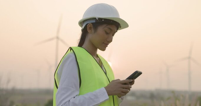 Portrait of female worker or asian woman engineer working with mobile phone at wind turbine farm. Wind power turbines generating clean renewable energy for sustainable development.