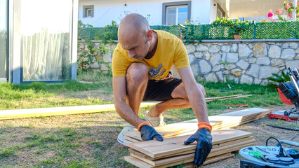 A middle-aged man repairing with timber in the garden of his house on a summer day