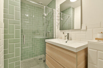 A contemporary bathroom featuring elegant green tiles and a sleek wooden vanity, showcasing a blend of modern aesthetics and comfort in a clean environment.
