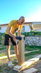 A middle-aged man repairing with timber in the garden of his house on a summer day