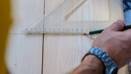 A middle-aged man measures with a tape measure to make repairs with lumber in his garden on a...