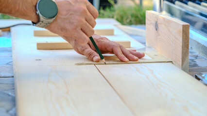A middle-aged man measures with a tape measure to make repairs with lumber in his garden on a...