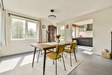 A stylish dining area featuring a wooden table, chairs, and large windows allowing ample daylight, creating a cozy and inviting atmosphere.