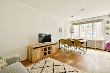 A contemporary living room featuring a wooden TV stand, elegant seating, and natural light flooding through large windows, creating a welcoming space.