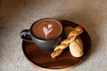 Steaming mocha with latte art and poppy seed pastry on wooden tray