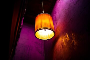 A single warm-toned pendant lamp illuminates a textured purple wall, creating a moody and atmospheric scene.