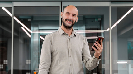 A middle-aged, fair-skinned businessman is in an empty office environment with a blurred background, focusing on his mobile phone