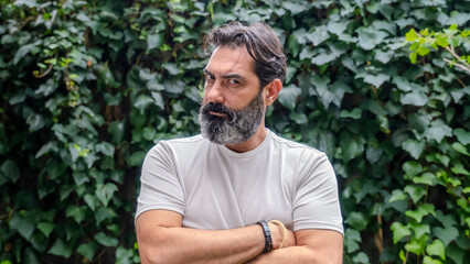 A middle-aged, fair-skinned, bearded man looking at the camera with an angry expression in a close-up shot, outdoors in a wooded area