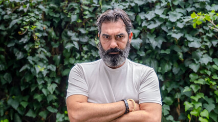 A middle-aged, fair-skinned, bearded man looking at the camera with an angry expression in a close-up shot, outdoors in a wooded area