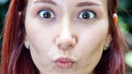 A very close-up headshot of a young woman making funny facial expressions while looking at the camera