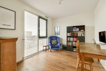 Bright and airy room featuring a blue chair, wooden flooring, and a bookshelf filled with books, creating a cozy reading nook.