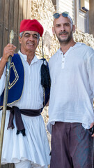 A middle-aged male tourist posing with a man dressed in traditional clothing on a summer day