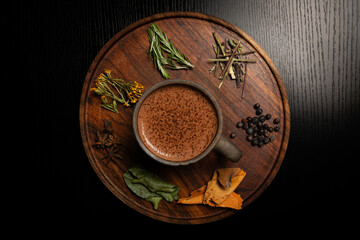 Aromatic hot chocolate surrounded by herbs and spices on wooden tray