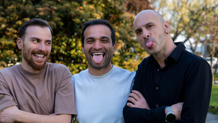 Close-up portrait of three middle-aged men making silly faces in a wooded area, their playful...