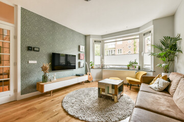 A stylish modern living room featuring a comfortable sofa, a decorative rug, and large windows allowing natural light. The decor is minimal yet inviting, perfect for relaxation.