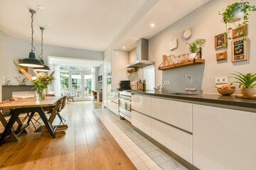 A contemporary kitchen featuring sleek cabinetry, a wooden dining table, and ample natural light flowing through large windows, creating an inviting atmosphere.
