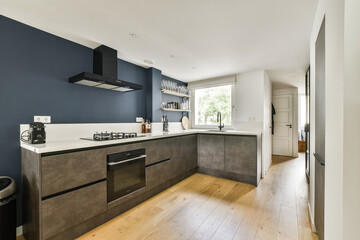 A sleek modern kitchen featuring a minimalist design with dark blue walls, stylish cabinets, and natural lighting from a window.