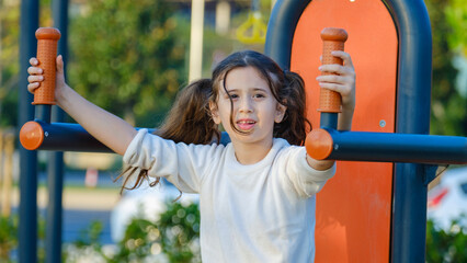Fototapeta premium A cute little girl child joyfully playing in a children's park surrounded by trees on a fall day