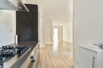 A sleek, modern kitchen featuring stainless steel appliances and wooden flooring, opening into a well-lit hallway. The design emphasizes minimalism and spaciousness.