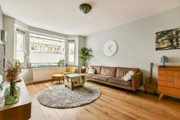 A stylish modern living room featuring a cozy sofa, decorative plants, a round rug, and natural light streaming through large windows.