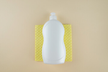 White bottle of dishwashing liquid and yellow sponge on beige background. Top view.