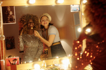 Two friends bonding in dressing room while applying makeup together and laughing. Bright lights creating a warm and joyful atmosphere, reflecting their happy and carefree mood