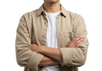 person wearing a beige button-up shirt over a white t-shirt stands with arms crossed against a plain isolated background,