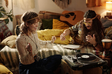 A couple immersed in listening to music in a cozy bohemian-style living room. Seated on a comfy couch, adorned with colorful cushions, and surrounded by musical instruments
