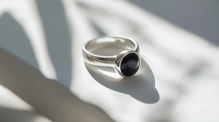 A minimalist silver ring with a black onyx stone in the center, resting on a pure white background