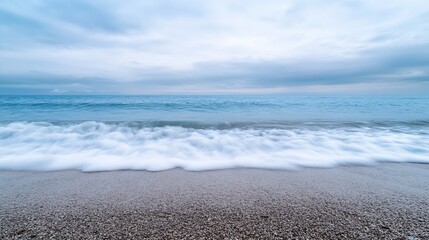Fototapeta premium Panoramic view of gentle ocean waves crashing onto a serene sandy beach under cloudy skies : Generative AI