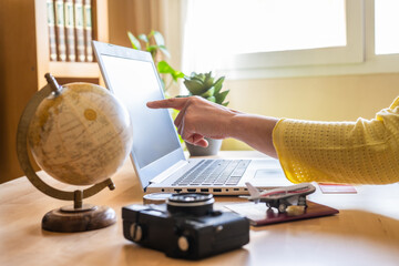 Woman pointing at laptop screen while planning a trip on a booking website, surrounded by a globe,...