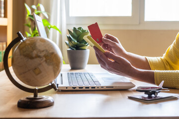 Woman using laptop and smartphone with credit card, booking a trip, with a globe, passport, and airplane model on the desk, planning her next vacation © Nanci