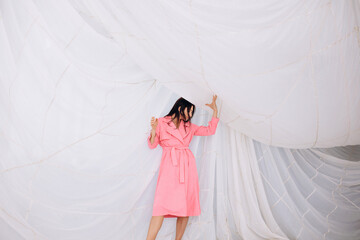 Beautiful adult young female model in the studio on the background of a parachute in a pink coat