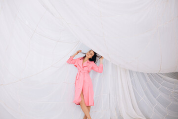 Beautiful adult young female model in the studio on the background of a parachute in a pink coat