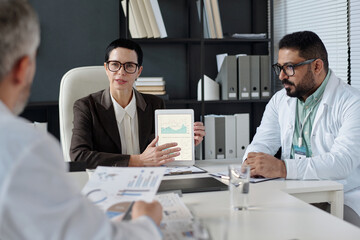 Fototapeta premium Front view portrait of serious mature woman presenting data report during medical conference and pointing at statistics graph on tablet screen copy space